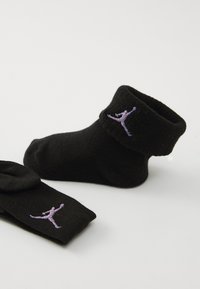 Svarte sokker med brett topp, med en lavendel Jumpman-logo. Laget av mykt stoff, har de en enkel, glatt tekstur.