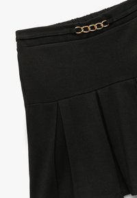 Sort nederdel med plisseret design, lavet af blødt stof. Har en livrem med en guld kæde accent øverst.