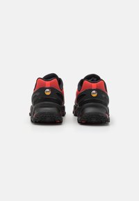 Baskets de sport noires et rouges avec une tige en mesh, une semelle texturée et un amorti à air visible dans le talon. Présentent un badge logo à l'arrière.