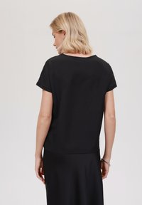 Top corto nero a maniche corte con una vestibilità rilassata, texture liscia e scollatura rotonda. Il tessuto appare leggero e adatto per il layering.