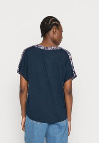 Camisa azul-marinho de manga curta com detalhes em padrão floral nos ombros, com um corte descontraído e decote redondo.