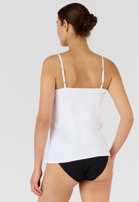 Witte cami-top met dunne verstelbare bandjes, voorzien van een gladde textuur. Gecombineerd met zwarte onderkleding, wat zorgt voor een simpele en minimalistische uitstraling.
