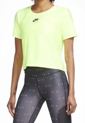 Person trägt ein neon-gelbes Nike Air kurzärmeliges Shirt und schwarze Leggings mit buntem "AIR"-Schriftzugmuster.