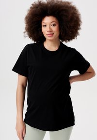 Sort kortærmet t-shirt i blødt materiale med klassisk rund hals. Modellen poserer med hænderne på hoften og viser en afslappet pasform.
