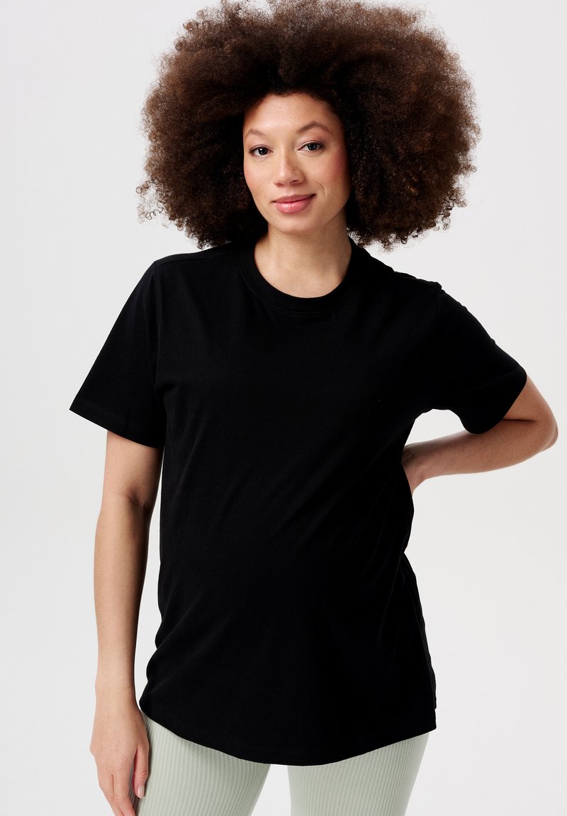Sort kortærmet t-shirt i blødt materiale med klassisk rund hals. Modellen poserer med hænderne på hoften og viser en afslappet pasform.