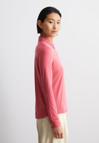 Langermet polo skjorte i korall, laget av myk tekstil. Har en knappestolpe og mansjetter, med en slank passform og minimalistisk design.