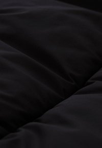 Musta toppaustekstiili, jossa näkyvät ommellut saumat ja pehmeä, sileä pinta, joka luo lempeitä laskoksia ja varjoja.