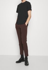 Svart bomull t-shirt i kombination med bruna slim-fit byxor. Svarta läderskor fulländar outfiten och ger ett elegant, samordnat utseende.