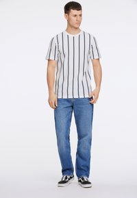 Randig vit och marinblå t-shirt med korta ärmar, i kombination med blå jeans och svarta sneakers. Enkel design, avslappnad passform och lätt textur.