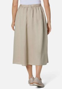 Beige, knielanger Rock aus leichtem Stoff mit gerafftem Taillenbund. Getragen mit hellen, strukturierten Sneakers.