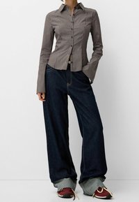 Raitapaita ruskeassa ja beigen värissä, yhdistettynä leveälahkeisiin tummansinisiin farkkuihin. Korostettu punaisilla ja beigen värisillä lenkkareilla.