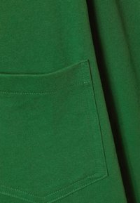 Green cotton fabric with a textured, ribbed surface; features a patch pocket with stitched edges.