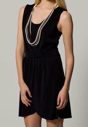 Robe noire avec un corsage ajusté et un ourlet asymétrique. Fabriquée en tissu doux, elle présente une taille froncée et un décolleté superposé, accompagnée d'un collier de perles à plusieurs brins.