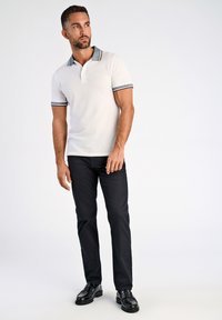 Vit polo med grå krage och randiga ärmar, tillsammans med mörka byxor och svarta loafers. Enkelt mönster med kontrasterande detaljer.