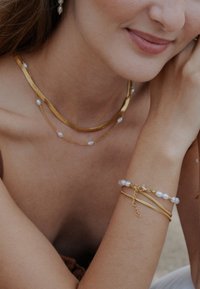 Złota biżuteria z warstwowanymi łańcuchami i perłowymi akcentami. Zawiera bransoletkę z perłami i delikatnym zapięciem. Gładkie faktury i wyszukany design.