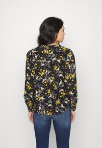Blusa floral de mangas longas, fundo preto, flores amarelas e roxas, decote redondo e um corte solto com detalhe gathered nas costas.