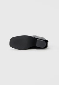 Sole in gomma nera con un motivo testurizzato, caratterizzata da una parte superiore liscia e un design elegante e slanciato. Ideale per vari stili di calzature.
