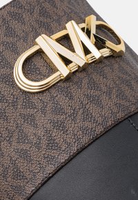 Logo CNZ ton or sur surface texturée en cuir marron et noir du sac, vue rapprochée d’un détail d’accessoire de luxe.