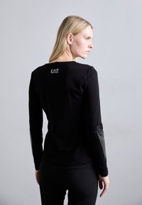 Sort langærmet t-shirt med rund hals, glat stof og dekorative sølvdetaljer langs ærmerne med et logo på ryggen.