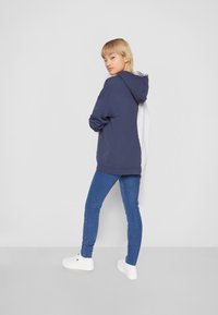 Felpa con cappuccio in blu navy e grigio con una vestibilità rilassata; abbinata a jeans blu slim e sneaker bianche. Tessuto morbido e design semplice.