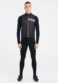 Sort isoleret vest med en lys grå stribe og brun lynlås, parret med sorte tætsiddende leggings og sorte sko med accenter.