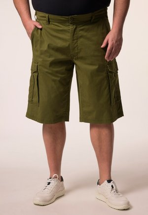 Mann trägt olivgrüne Cargoshorts und weiße Sneaker, steht mit den Händen nahe den Taschen vor neutralem Hintergrund.
