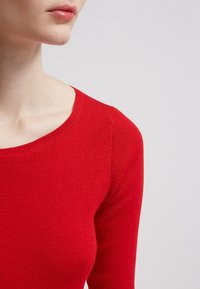 Maglione rosso a maglia con scollo tondo e maniche lunghe, caratterizzato da una texture liscia e un design aderente.
