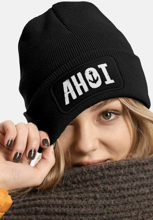 Black knitted beanie with a rectangular white patch featuring the text "AHOI" and an anchor design. Textured fabric, snug fit.