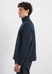 Marinblå tröja med hög krage, långa ärmar och rak skärning. Tillverkad av ett slätt, elastiskt tyg; har en minimalistisk design.