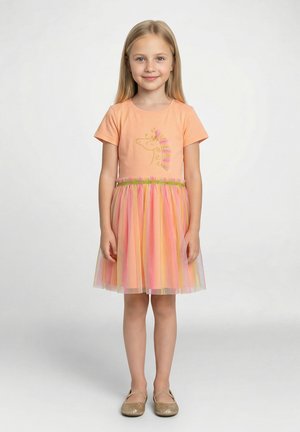 Pomarańczowa koszulka z nadrukiem jednorożca i złotymi akcentami, zestawiona z warstwową, pastelową spódnicą z tiulu oraz złotymi balerinami.
