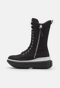 Botas altas negras de tela, con detalles de cremallera y ojales plateados, suela gruesa blanca y parte inferior de goma negra texturizada.