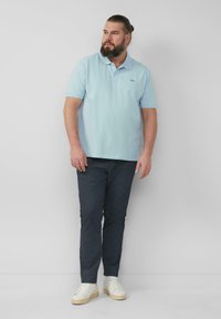 Lichtblauw poloshirt met een klassieke kraag, gecombineerd met marineblauwe slim-fit broek en witte sneakers. Het poloshirt heeft een klein logo op de borst.