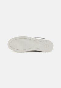Sola de sapatilha com uma base de borracha branca, apresentando sulcos texturizados para aderência e um design de calcanhar arredondado. Estética minimalista.