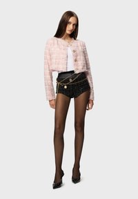 Pale pink tweed cropped jacket with gold buttons, paired with black shorts featuring a metallic chain and pearl detail, and black high heels.