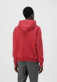 Roter Baumwollhoodie mit lockerer Passform, verstellbarem Kordelzug und gerippten Bündchen sowie Saum. Hat eine weiche, leicht strukturierte Oberfläche.