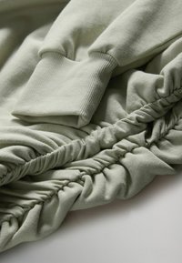 Vaaleanvihreä collegepaitakangas, jossa on resorit hihansuissa ja poimittu tekstuuri. Materiaali näyttää pehmeältä ja hieman teksturoidulta, rento tyyli.