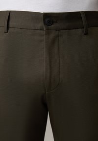 Dunkelolivgrüne Hosen aus einem strukturierten Stoff mit einem Frontknopfverschluss und Seitentaschen, maßgeschneidert für eine körpernahe Passform.