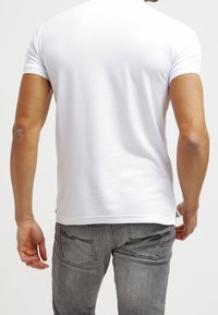 Vit t-shirt med kort ärm och slät yta, figurnära design och rundad halsringning, kombinerad med grå denimjeans som har bakfickor.