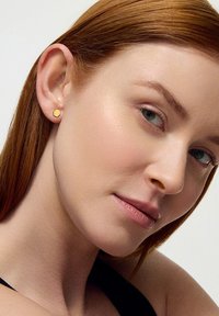 Złoty sześciokątny kolczyk wkrętka, mały rozmiar, gładka powierzchnia, minimalistyczny design, na neutralnym tle, noszony na uchu modelki.