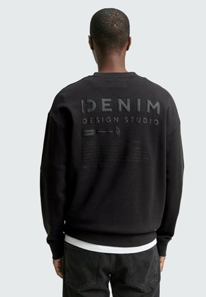 Sweatshirt noir avec texte et graphismes en relief au dos. Fabriqué en tissu doux avec une coupe décontractée et un ourlet et des poignets côtelés.