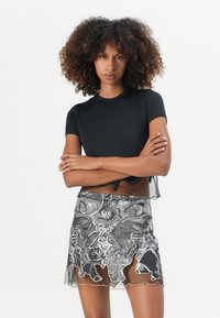 Schwarzes, kurzärmeliges Oberteil kombiniert mit einem grauen Rock, der ein wirbelndes, abstraktes Muster und einen gewellten Saum aufweist, was einen geschichteten Look kreiert.