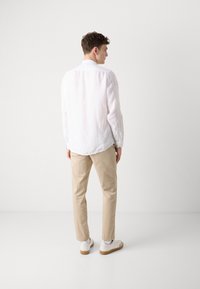 Lichtroze linnen shirt met een casual pasvorm, khaki tappered broek, en witte sneakers met gumzolen, gezien vanaf de achterkant.