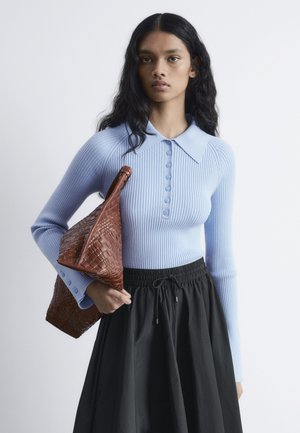 Hellblau gestreiftes Strickoberteil mit langen Ärmeln, Knopfleiste und großem Kragen, kombiniert mit einem schwarzen Rock mit Kordelzug und einer geflochtenen braunen Tasche.