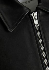 Close-up of black leather jacket collar with silver zipper partially zipped, showing smooth texture and neat stitching.