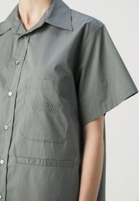 Chemise grise à manches courtes, boutonnée, avec un col et une poche poitrine brodée de chiffres et d'un "6" cerclé.