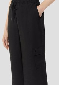 Schwarze Hose aus leichtem Stoff, mit einem elastischen Bund, Seitentaschen und einer Cargo-Tasche am linken Bein mit einem dezenten Logo.