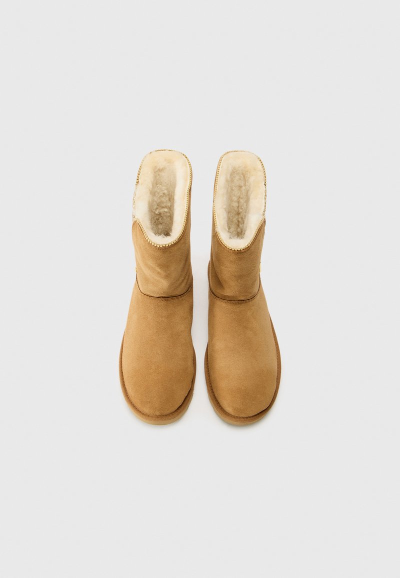 Beige Wildleder-Ankleboots mit einem weichen Schaffellfutter, runder Zehenpartie und gestickten Nähten entlang der Nähte. Gummisohle sichtbar an der Unterseite.