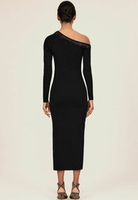 Robe midi noire ajustée, une épaule et manche longue. Le décolleté présente des détails en perles. Texture lisse, tissu côtelé.