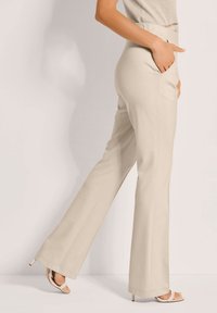 Beige flared broeken van soepele stof, met zijzakken en een iets losser pasvorm, gecombineerd met sandaaltjes met hoge hakken.
