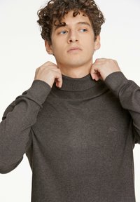 Mörkgrå polo-tröja med ribbad krage och manschetter. Har en diskret logotypdetalj på bröstet. Tillverkad av ett mjukt, texturerat tyg.